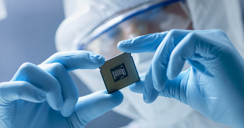 Modern Electronic Manufacturing Factory Engineer in Sterile Coverall Holds Microchip